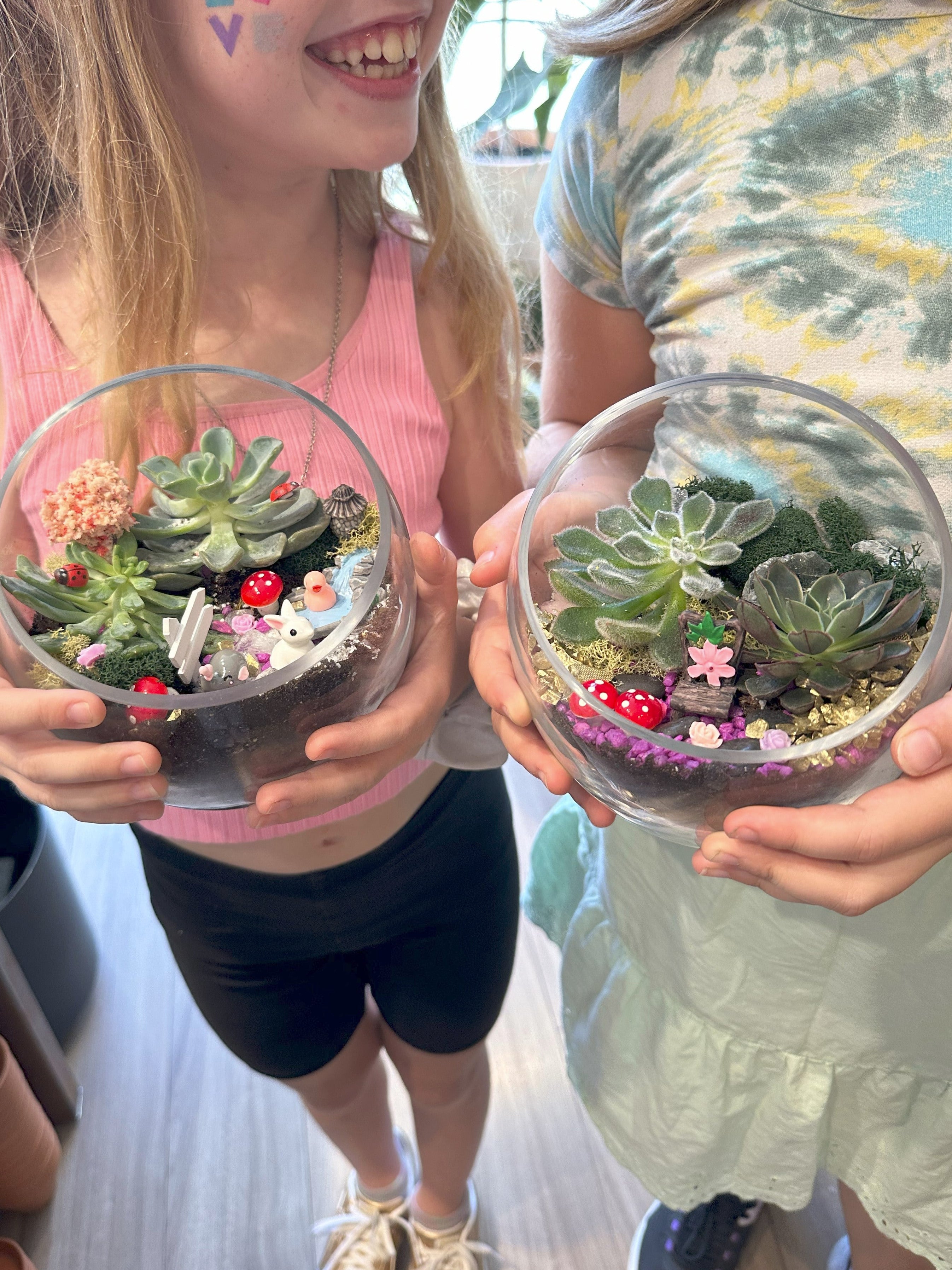 Two children holding small terrariums with plants and decorative elements.
